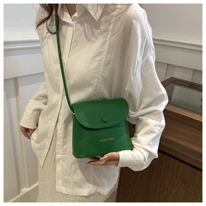 Detail of green minimalist crossbody bag with gold fashion text and snap closure
