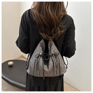 Detail eines grauen Rucksacks mit roten Punkten, Reißverschlüssen und Lederschleifen