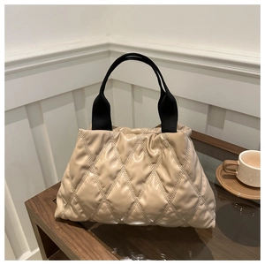 Détail du sac fourre-tout matelassé beige avec design froncé et poignées noires sur table