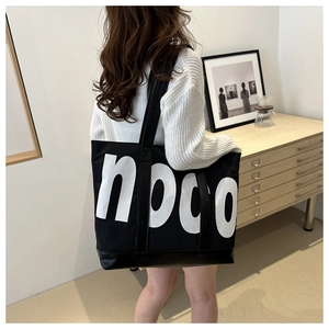 Detail view of a large black canvas tote bag with white noco lettering on a model shoulder