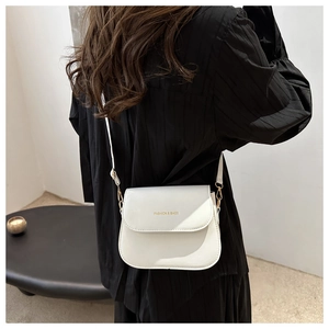 Close-up of a white leather crossbody saddle bag with gold logo text on black outfit