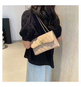 Beige quilted shoulder bag with gold chain strap worn by a model in a minimalist setting