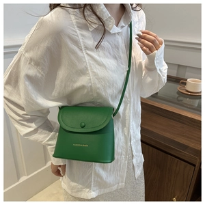 Detail of a bright green bucket bag with a round buckle and gold fashion slogan lettering