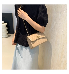 Close-up of beige quilted crossbody bag with gold chain strap and metal lock detail