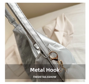 Detail of silver metallic tote bag showing gold hardware hook and white plush ball charm