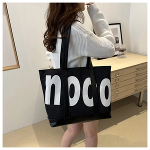 Detail of black canvas tote bag featuring white noco lettering and durable PU leather base