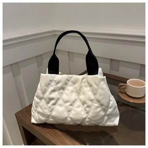 Détail du sac cabas matelassé blanc avec anses noires posé sur une table en bois