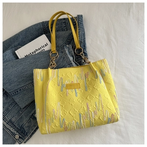 Détail du sac cabas jaune avec texture matelassée et broderies de vagues colorées sur blanc