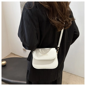 Detail of white PU leather saddle bag with gold lettering shown on a model