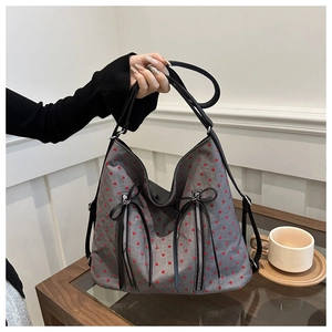 Detail of grey heart-patterned tote bag with metal zippers and black leather bows