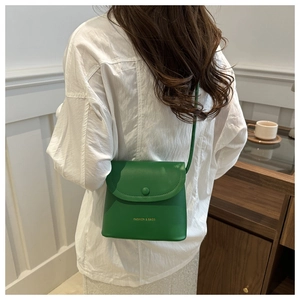 Green leather mini bucket bag with gold fashion text worn by a model against white wall