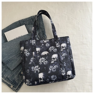 Flat lay of navy blue skull tote bag with floral patterns on white textured fabric