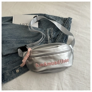 Close-up of silver crossbody bag with pink embroidered letters and woven zipper pull