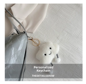 Close-up of white plush cloud keychain with embroidered smile and golden metal clasp