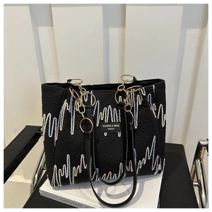 Détail du sac cabas noir en toile avec broderie vague et anneau doré brillant