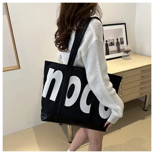 Detail of a black canvas tote with white noaa print and reinforced leather bottom strap