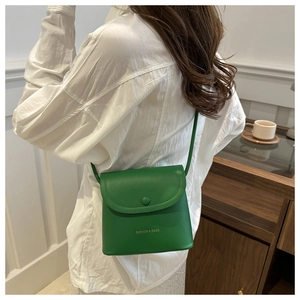 Green leather crossbody bag styled on shoulder showing compact square design and gold logo
