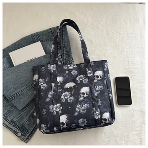 Flat lay of a skull and blue floral tote bag next to a denim jacket and phone
