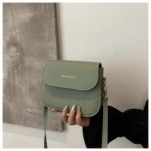 Detailed macro view of green minimalist saddle bag with gold-tone metal hooks and lettering