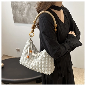 Détail du sac plissé blanc avec bandoulière en perles de bois porté par un modèle
