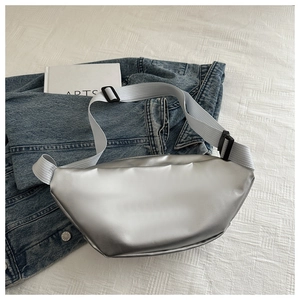 Detail of silver metallic crossbody bag with adjustable white strap on denim background