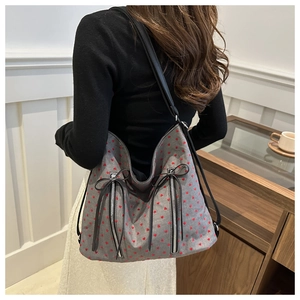Detail of gray tote bag with red heart pattern, zippers, and black bow charms