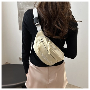Close-up of cream nylon crossbody bag with letter embroidery and woven zipper pulls