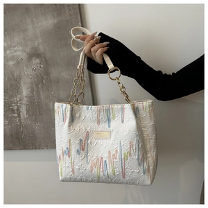 Détail du sac cabas blanc gaufré avec rayures colorées et plaque de marque dorée