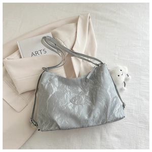 Silver-grey wrinkled tote bag detail with logo patch and fluffy cloud pendant on blazer
