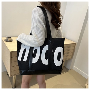 Detail of a large canvas tote bag with bold HOCO letter print and black leather straps