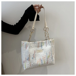 Détail du sac cabas blanc avec broderie arc-en-ciel et poignée en chaîne dorée
