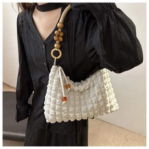 Détail du sac plissé blanc cassé avec bandoulière en perles et pendentifs ambre