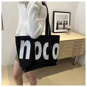 Detail of a large black canvas tote bag with bold white noco letters on a leather base