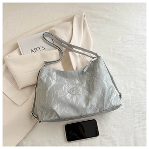 Detail of silver hobo bag with crinkle texture and logo next to a blazer and book