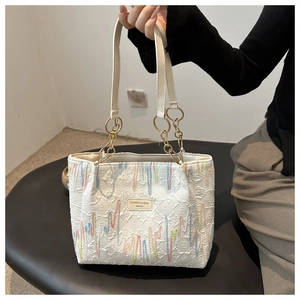 Détail du cabas en toile blanche avec broderie ondulée, plaque de marque et chaîne