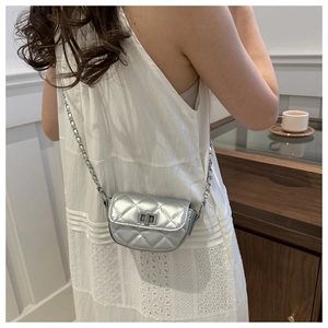 Sac bandoulière argenté à matelassage sur un mannequin portant une robe blanche chic