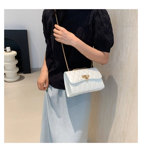 Close-up of white quilted crossbody bag with gold chain strap worn by a model