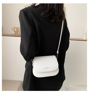 Close-up of a white PU leather saddle bag with fashion text detail on black blazer