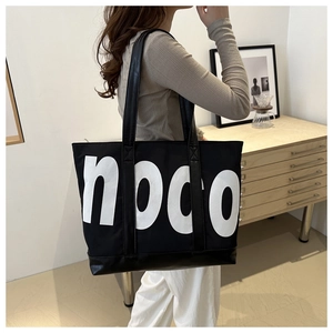 Large black tote bag with white noco lettering shown on model in a modern interior