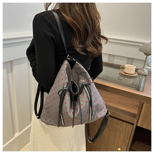 Detail of grey canvas backpack featuring red heart prints and black leather bow accents
