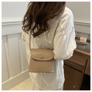 Fashionable minimalist beige crossbody bag shown on a model in a cozy indoor setting