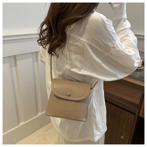 Detail of a cream minimalist crossbody bag with gold embossed logo and magnetic snap closure