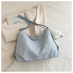 Close-up of light blue wrinkled tote bag featuring an oval logo and cloud charm on a blazer