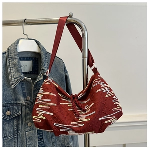 Detail of burgundy fabric shoulder bag with yellow wave embroidery and rope knot