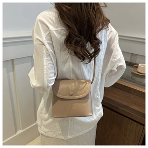 Detail view of khaki square shoulder bag worn by model, showing size and texture
