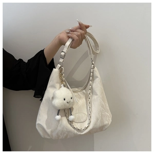 Detail view of white shoulder bag featuring a metal chain and a cute cloud plush charm