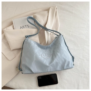 Detail of light blue pleated tote bag with brand logo patch on beige suit jacket