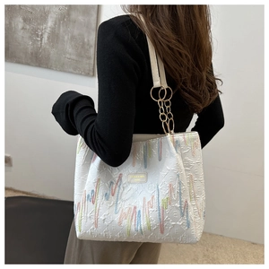 Détail des broderies verticales colorées et de la plaque de marque sur le sac blanc