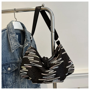 Detail of black canvas dumpling bag featuring colorful wavy stripe embroidery and strap