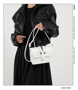 Close-up of white leather crossbody bag with decorative gold zipper and metallic buckle